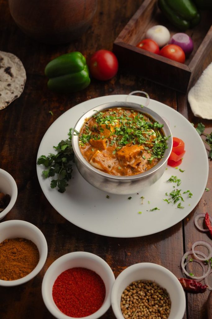 Close-up of a flavorful Indian curry with fresh vegetables and spices on a wooden table.