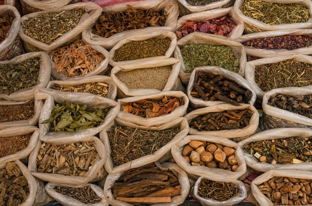 Bags filled with various dried herbs and spices displayed in a traditional market setting.