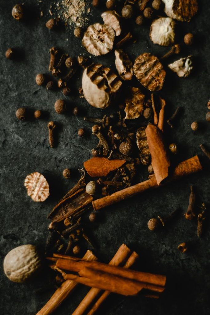 A close-up of a variety of spices including cinnamon and peppercorns on a dark surface.